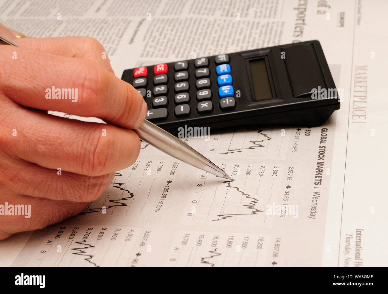 Maschio di mano che tiene una penna con una calcolatrice e studiando i mercati azionari grafici, il concetto di investimento Foto Stock