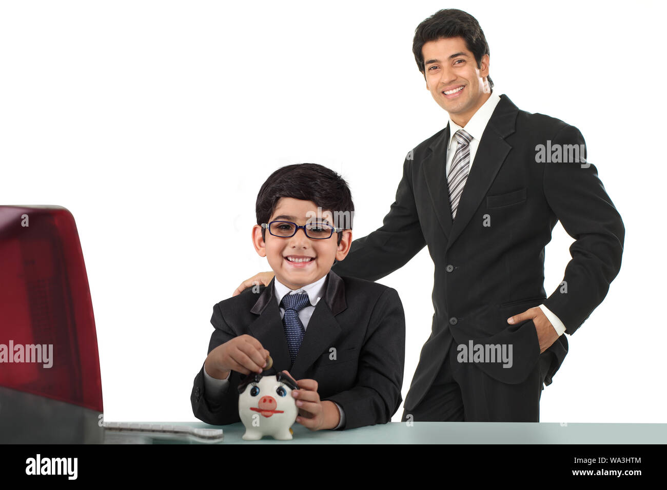 Ragazzo imitando come un uomo d'affari e mettendo la moneta in una piggybank con suo padre Foto Stock
