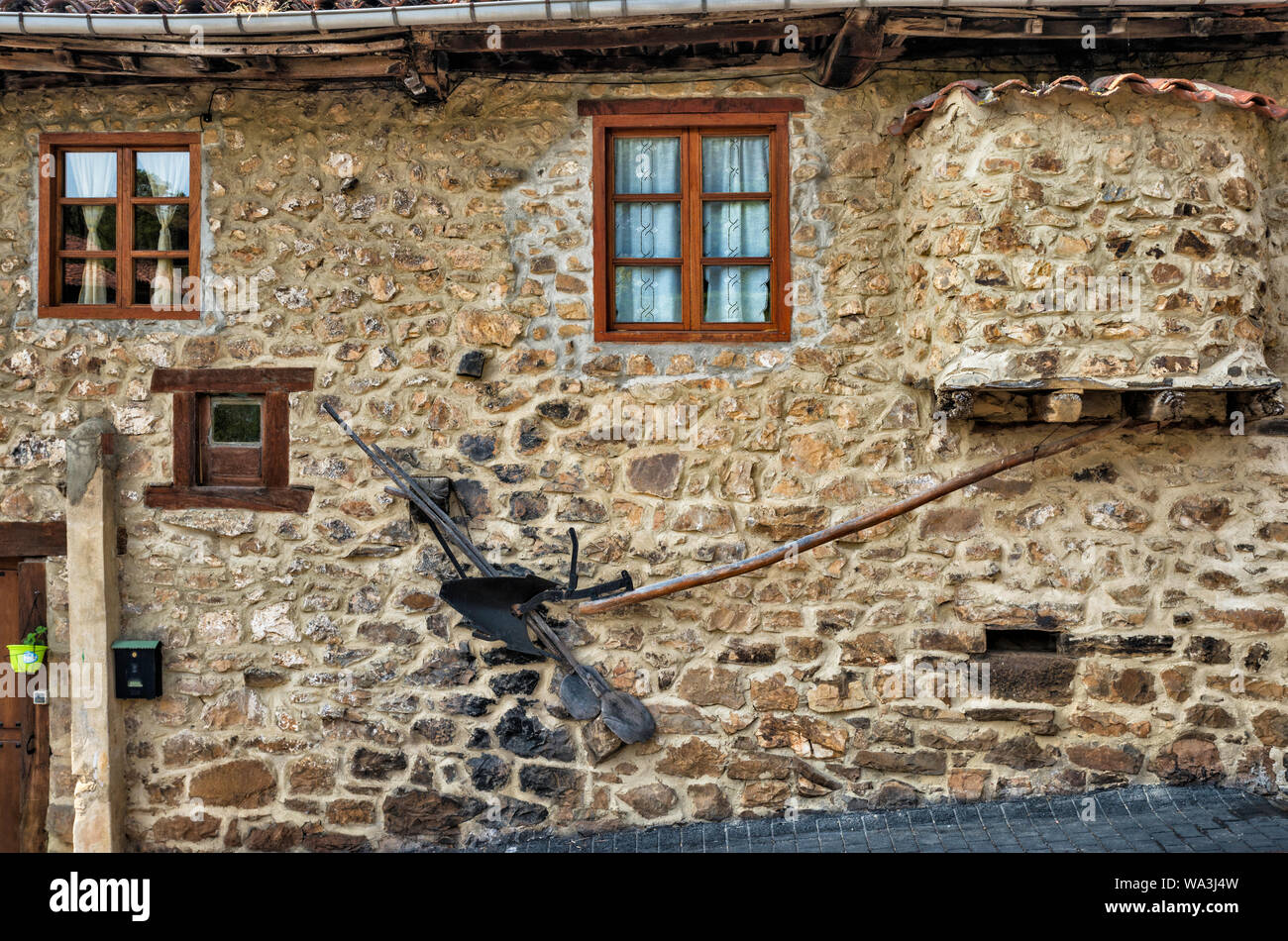 Antichi attrezzi agricoli in corrispondenza della parete di casa nel villaggio di Mogrovejo a Valle di Liebana, Macizo Central (Macizo Los Urrieles) a Picos de Europa, Cantabria, SPAGNA Foto Stock