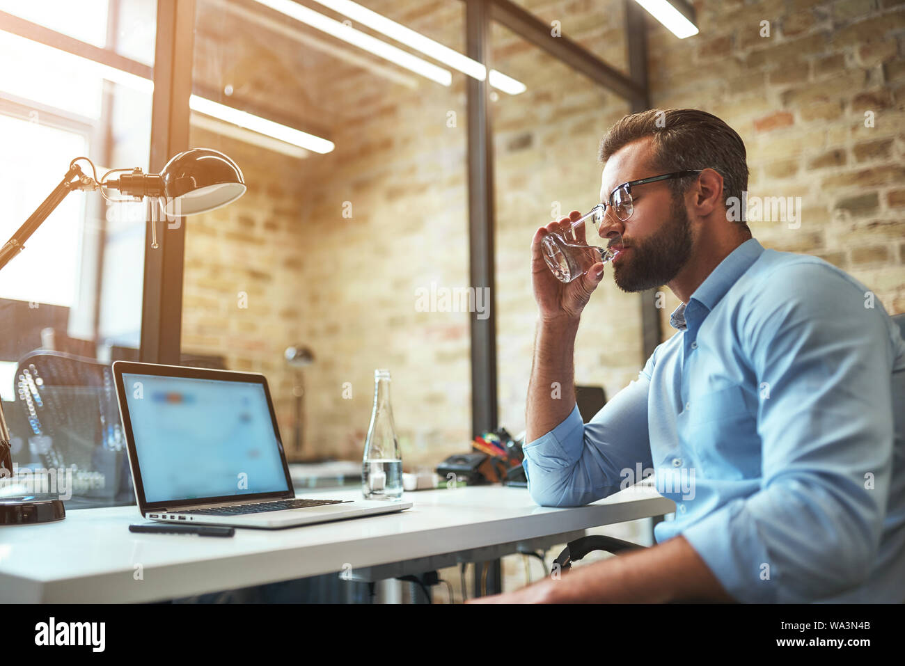 Ho bisogno di un po' di riposo. Sete barbuto imprenditore in occhiali e usura formale di bere acqua fresca mentre si lavora in un ufficio moderno. Il concetto di business. Concetto di lavoro Foto Stock