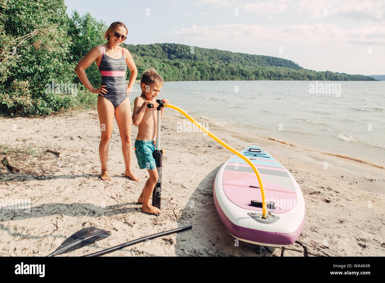 La donna caucasica madre figlio di insegnamento per gonfiare il sup surfboard con pompa sulla spiaggia. La famiglia felice infanzia lifestyle. Estate Natura outdoor singoli aq Foto Stock