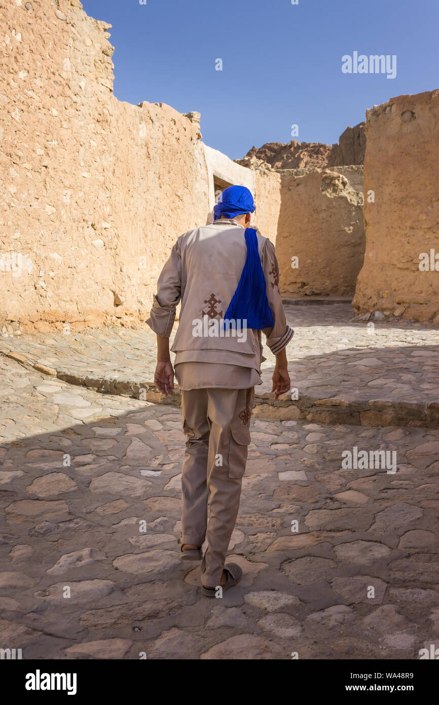 Arabo tunisino travel guide con sciarpa blu e costume tradizionale conduce la strada attraverso le rovine della fortezza di Chebika oasi nel deserto del Sahara Foto Stock