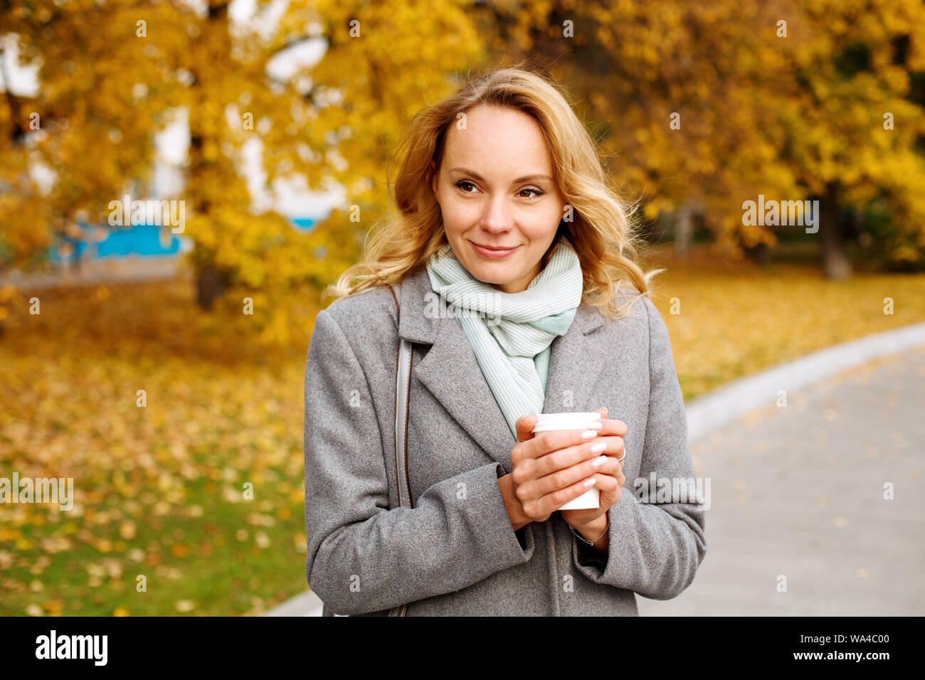Giovane donna sorridente tenendo calda tazza di caffè riscaldando le mani e guardando in lontananza Foto Stock