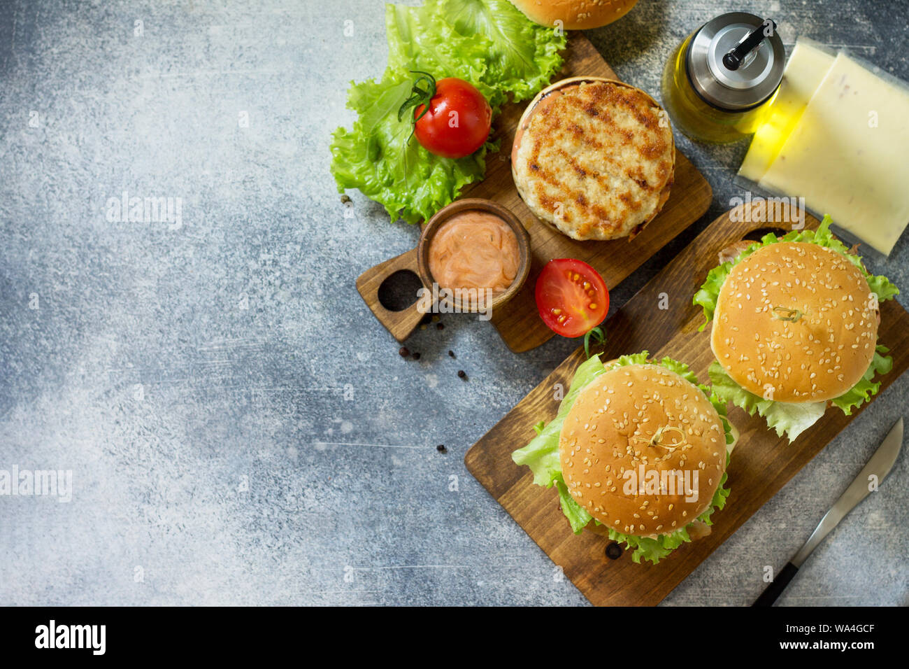 Deliziose grigliate di hamburger, hamburger panino con cotoletta di carne di pollo, formaggio fuso, pomodori e pancetta affumicata su una tavola di legno. Vista superiore piatta. laici Fre Foto Stock