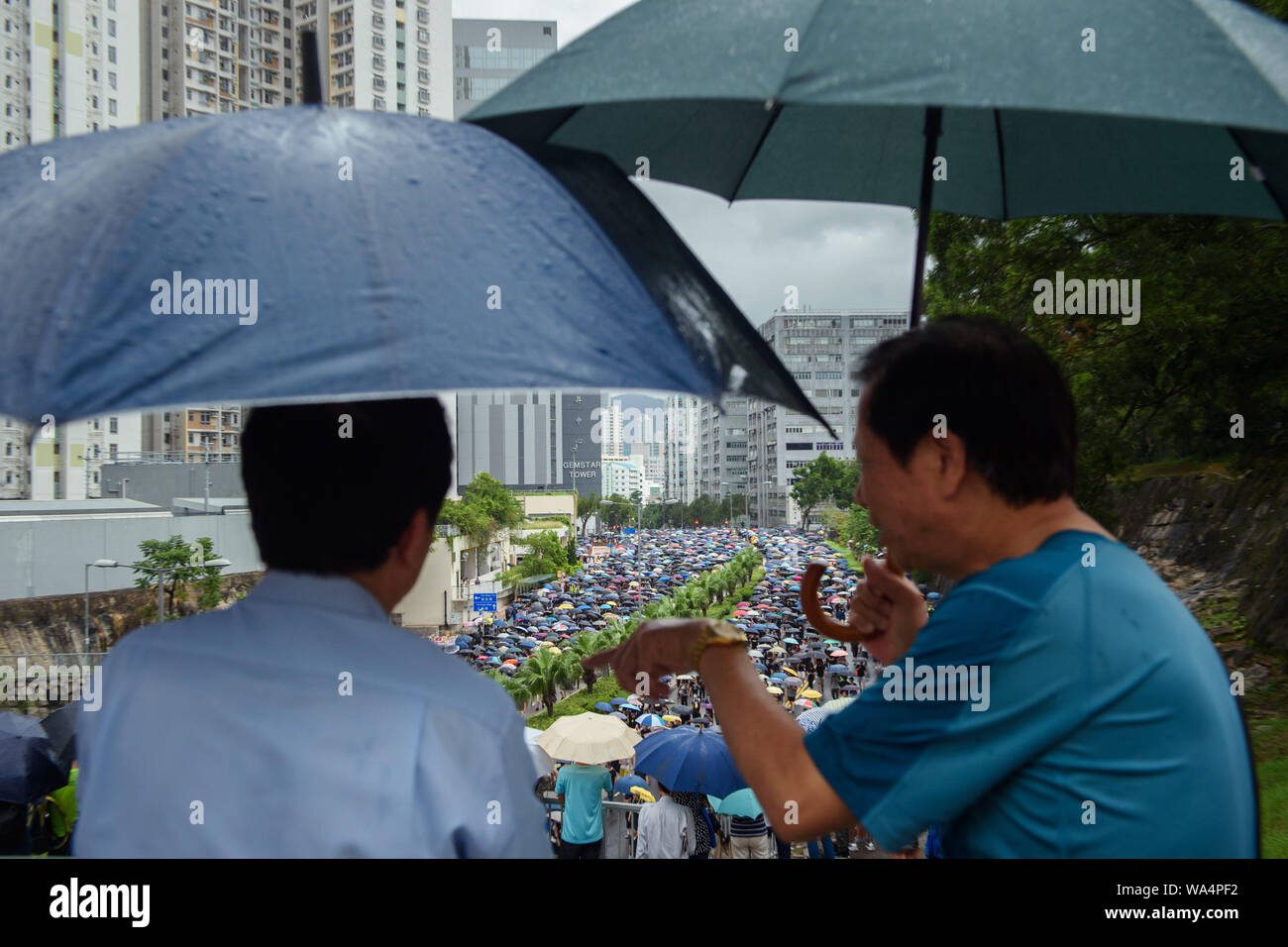 Hong Kong Cina. 17 Ago, 2019. Due uomini con ombrelloni guardare i partecipanti di una marcia di protesta attraverso la Hong Kong distretto di Kowloon. In Hong Kong vi sono state massicce proteste per più di due mesi. Le dimostrazioni sono state innescate da un disegno di legge del governo - ora in attesa - per l'estradizione di sospetti criminali in Cina. Credito: Gregor Fischer/dpa/Alamy Live News Foto Stock