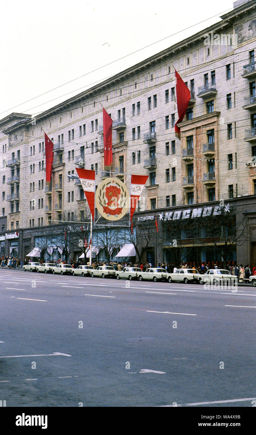 Grande falce e martello banner al di fuori di un edificio in Unione Sovietica alla fine degli anni settanta (1978), le righe di simili White Russian auto parcheggiata di fronte Foto Stock