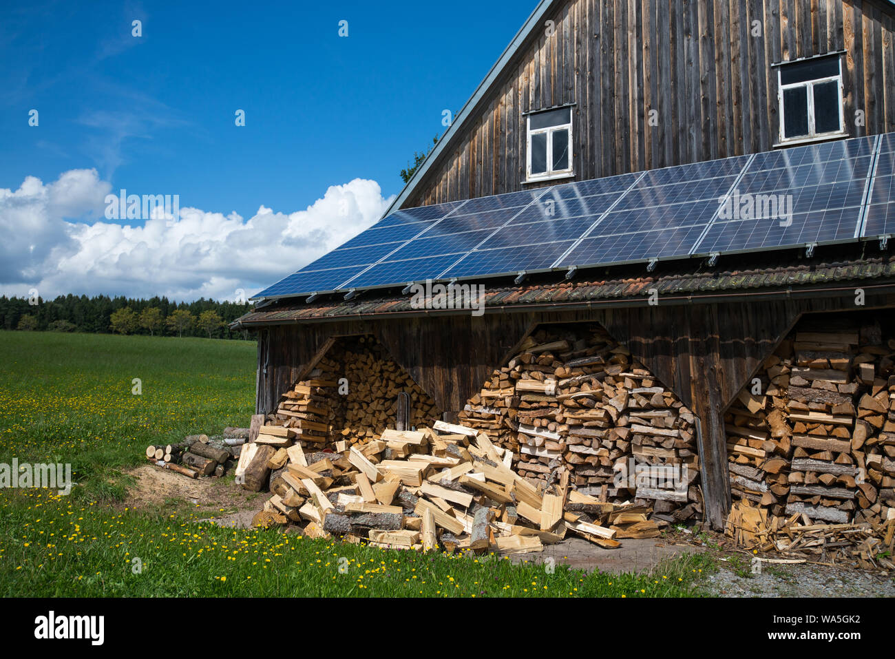 Pannelli fotovoltaici e legna da ardere pila in corrispondenza di un fienile in zona rurale Foto Stock
