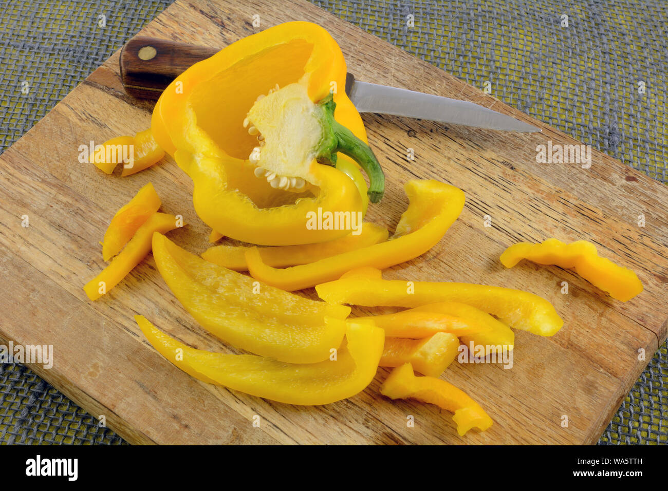 Crudo fresco peperone giallo fette e metà sul tagliere di legno con coltello da cucina Foto Stock