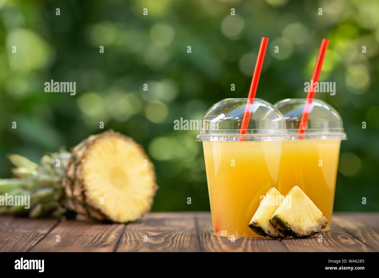 Ananas fresco succo in due in plastica monouso Tazze e aromi di frutta matura sul tavolo in legno all'esterno. Togliere il vetro con estate bevanda rinfrescante Foto Stock