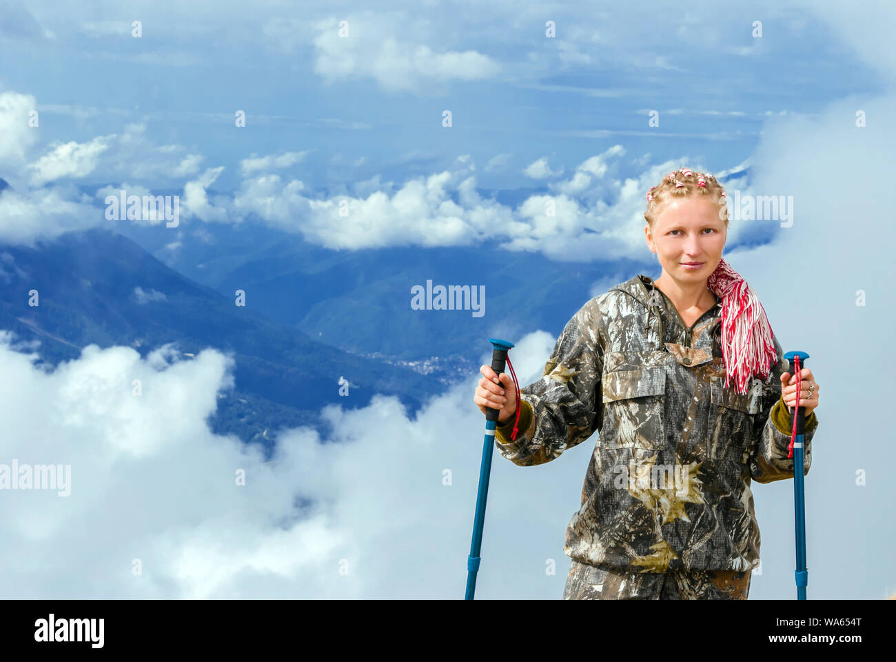 Giovane donna bionda in escursionismo vestiti con pali trekking in montagna su uno sfondo di nuvole Foto Stock