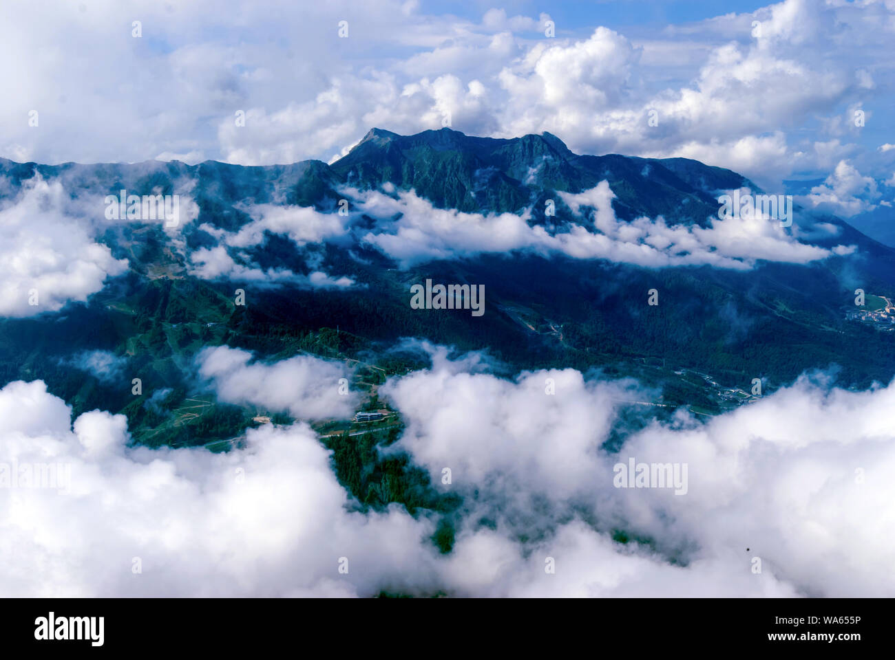 Vista da sopra, dal picco o da un aeroplano, una collina boscosa valle di montagna con insediamenti, parzialmente nascosto da cumuli di nuvole Foto Stock