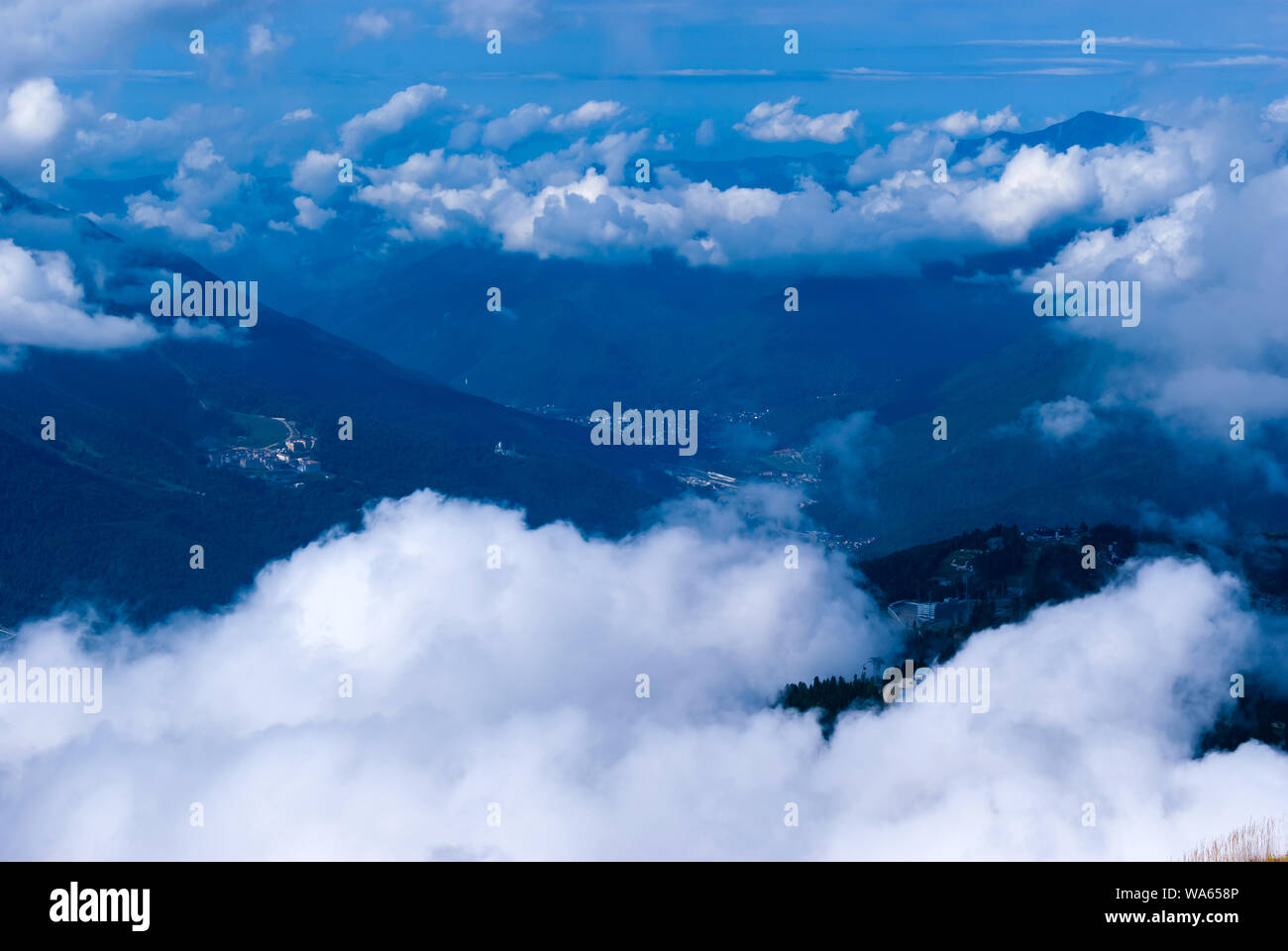 Vista da sopra, dal picco o da un aeroplano, una collina boscosa valle di montagna con insediamenti, parzialmente nascosto da cumuli di nuvole Foto Stock