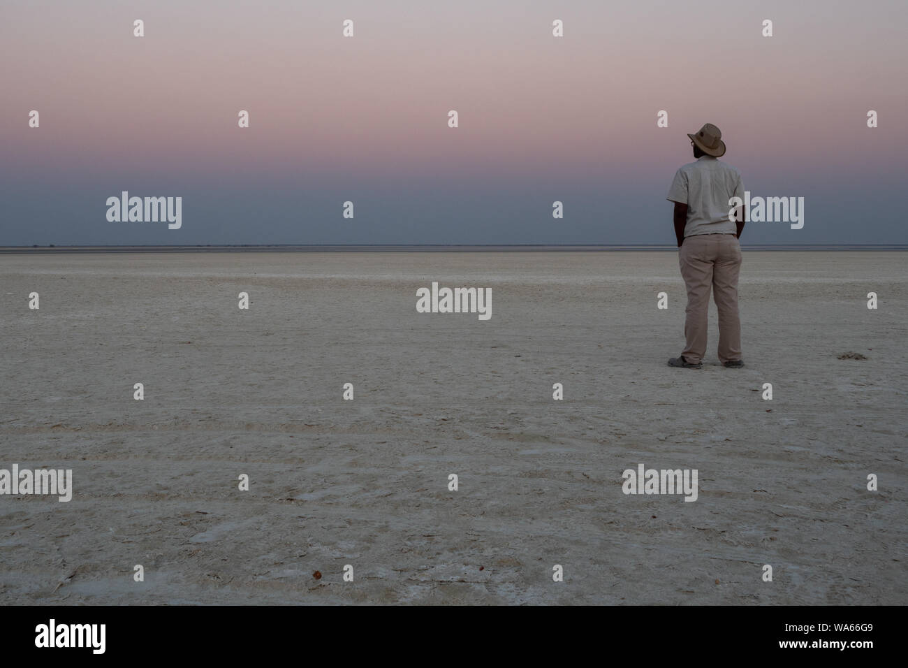 Tramonto in sale di Makgadikgadi Pan - Uomo nero, Ranger o guida con Hat fissando lo sguardo all orizzonte al Tramonto Romantico Foto Stock
