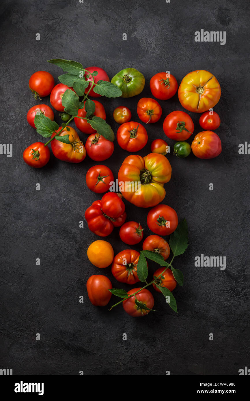 Lettera T realizzato con pomodori maturi su uno sfondo nero, creative laici piatto cibo sano concetto. Foto Stock