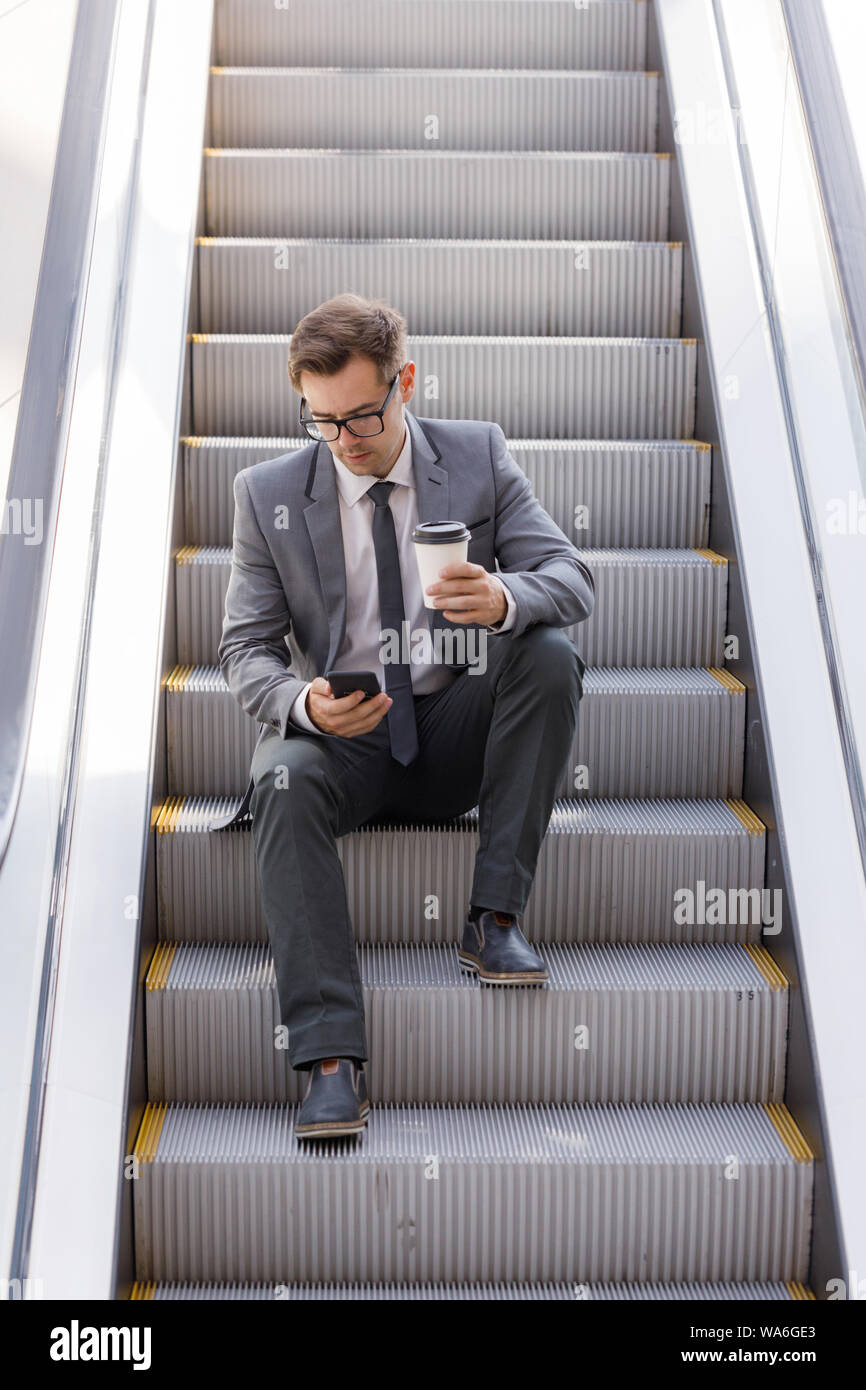 Imprenditore seduto su escalator navigando in rete e azienda caffè in mano Foto Stock