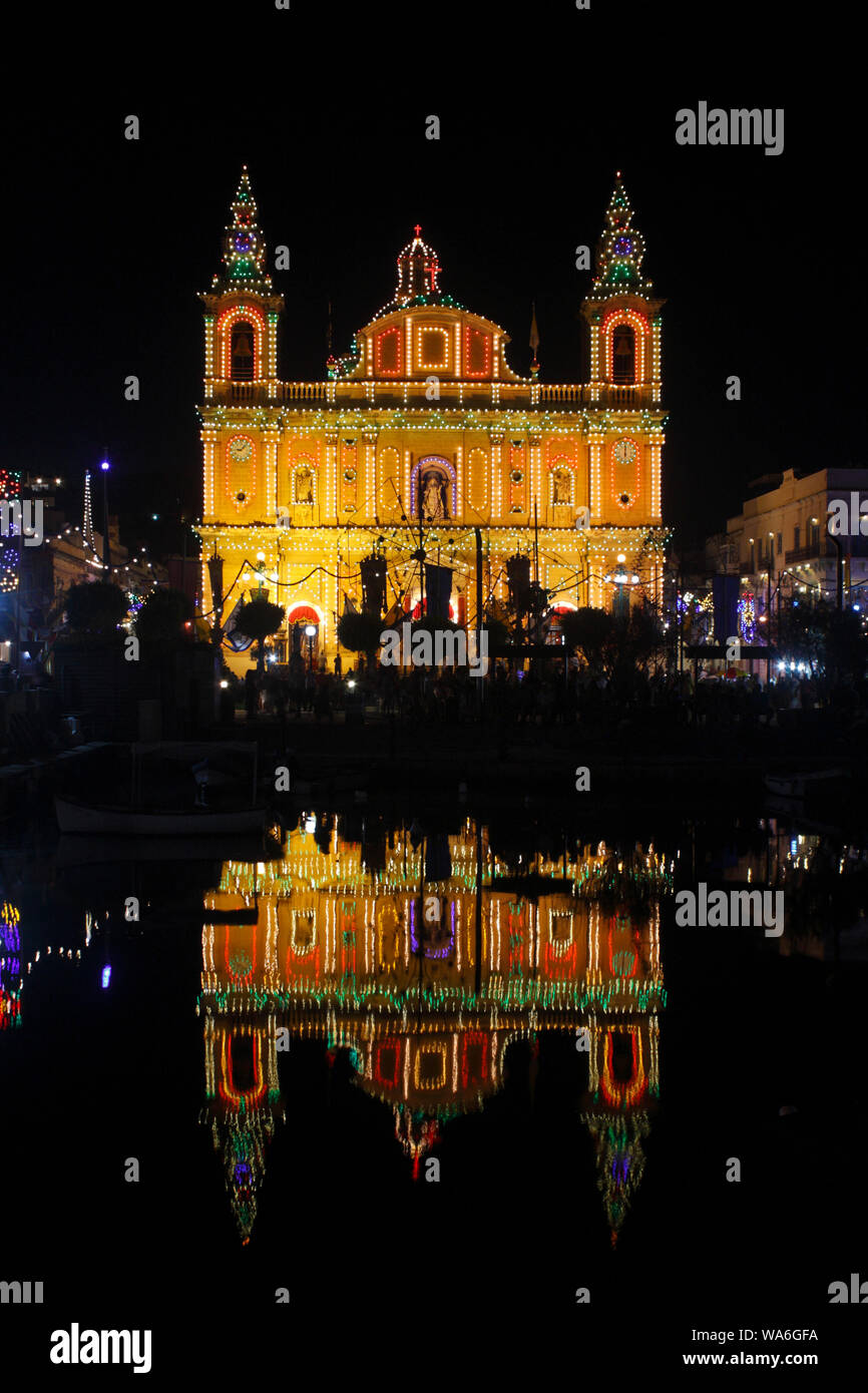 La chiesa parrocchiale a msida, Malta, con facciata illuminata a festa di San Giuseppe e riflessi nell'acqua di Msida Creek Foto Stock