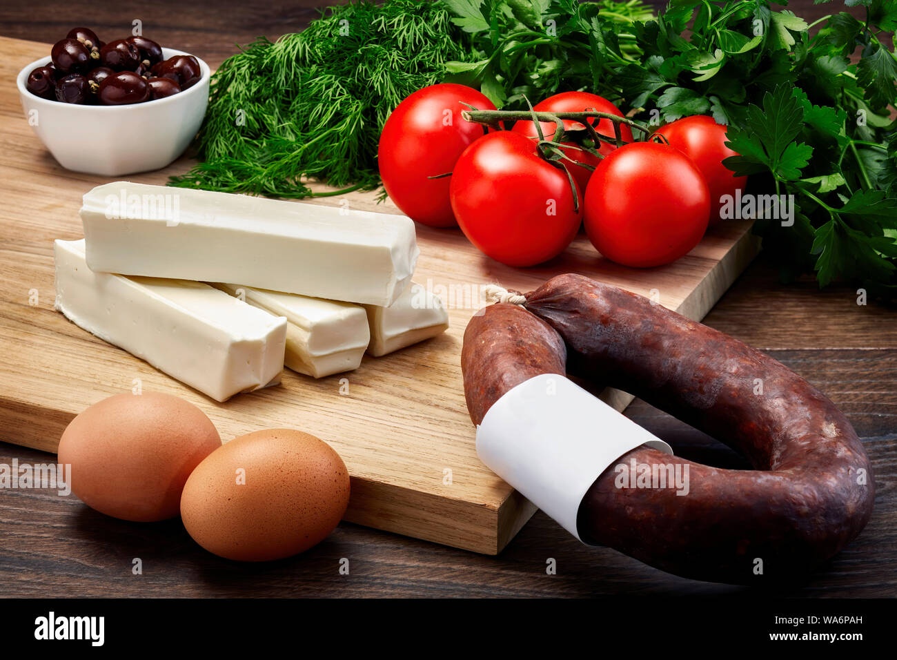 Stringa di turco il formaggio su un tavolo di legno con tagliere in legno con salsiccia fermentata, uova, olio d'oliva, prezzemolo e pomodori. Foto Stock