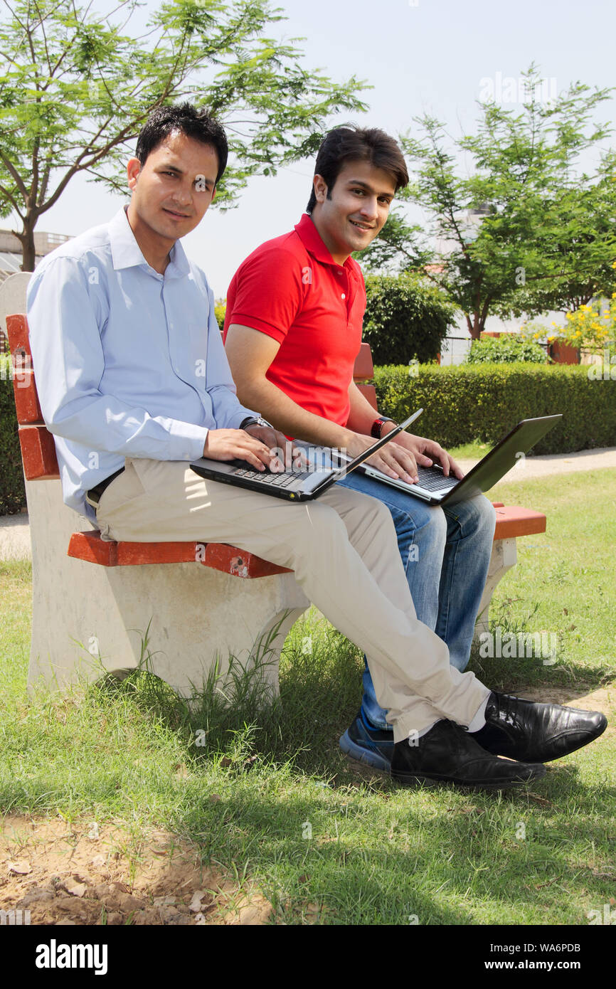 Giovani uomini seduti su panca e con computer portatili Foto Stock