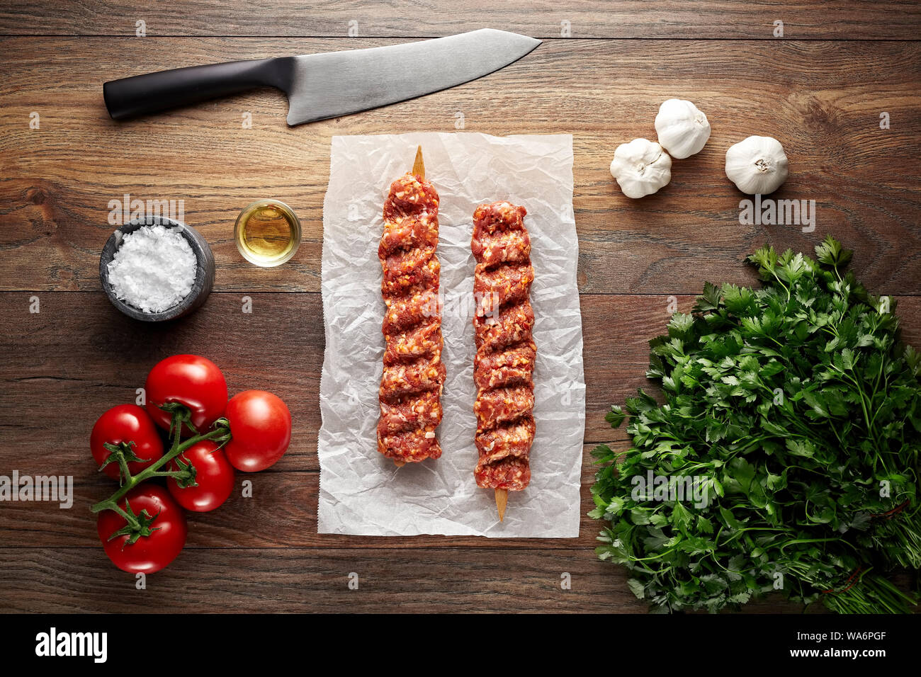 Materie Turkish Adana shish kebab sul bianco di carta di cottura e tavolo in legno. Decorate con le erbe aromatiche, le spezie e il coltello. Vista aerea. Foto Stock