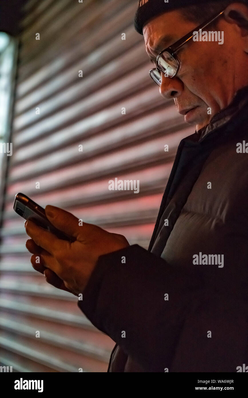 La città di New York New York, Feb 14, 2018: l'uomo guarda il suo smart phone davanti a un negozio griglia Foto Stock