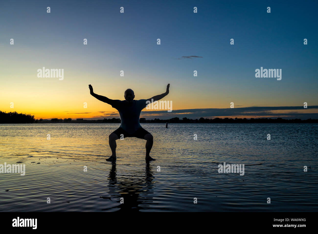 Sunrise silhouette di un uomo in piedi in acqua poco profonda e la pratica di chigong o tai chi movimenti, Boyd il lago del Parco statale nel nord del Colorado Foto Stock