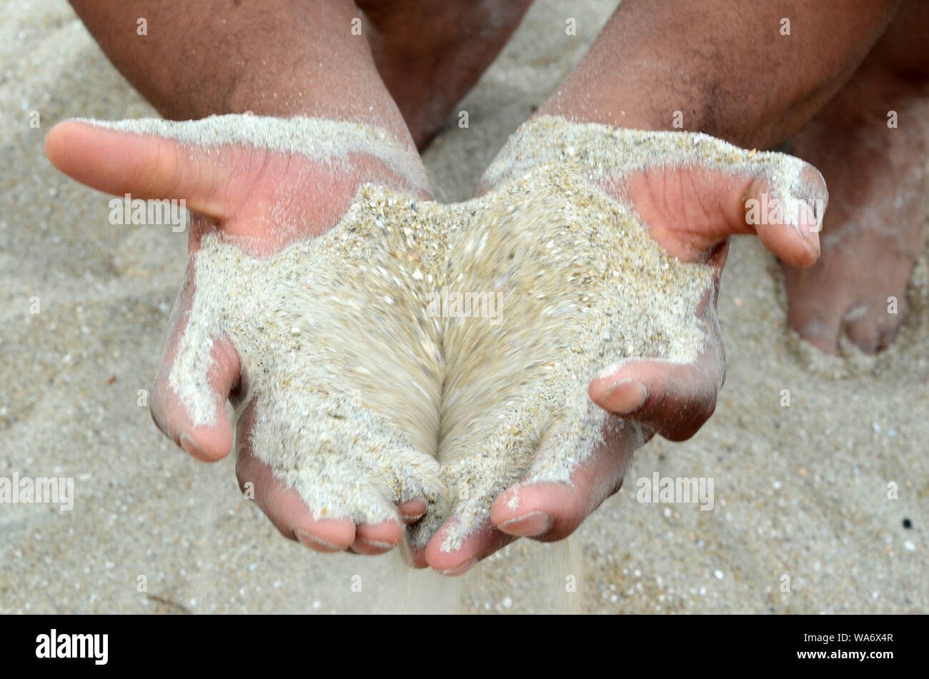 DNA Human: Un uomo e una donna che si accovacciano sulla spiaggia di Tybee hanno sabbia che si riversano attraverso le loro mani. Foto Stock