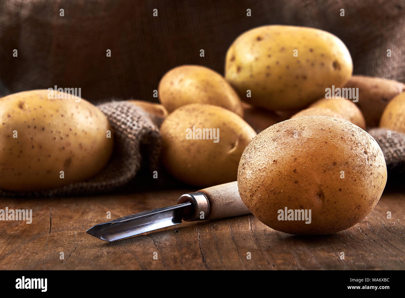 Vista della pila di patate primaticce con sacchetto in iuta sul tavolo in legno e con il raschiatore Foto Stock