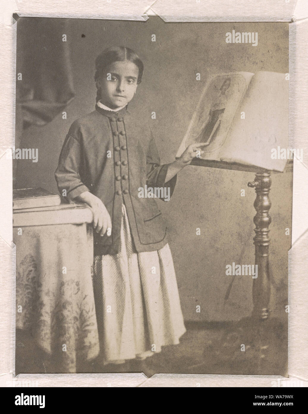 Adelina Patti e a piena lunghezza ritratto in studio, rivolto verso la parte anteriore, in piedi, con una tabella sulla sinistra e un music stand sulla destra, puntando con la sua mano sinistra a un ritratto di Jenny Lind stampato sul foglio di musica su il music stand Foto Stock