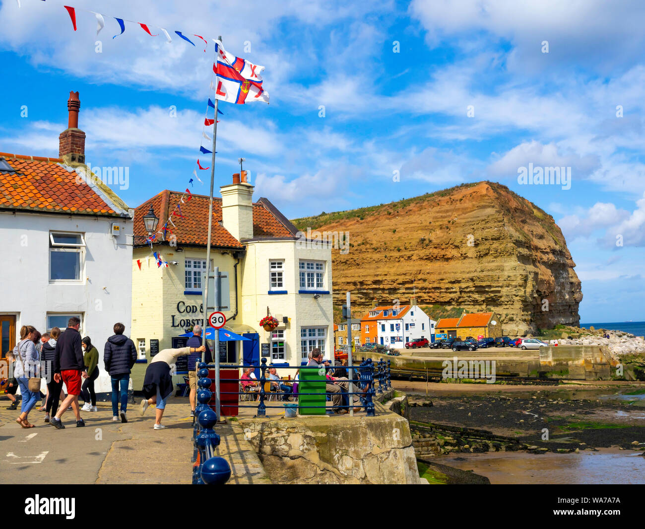 Al di fuori del merluzzo bianco e aragosta pub di fronte al porto a Staithes North Yorkshire in alta stagione con bunting e bandiere per RNLI scialuppa di salvataggio giorno Foto Stock