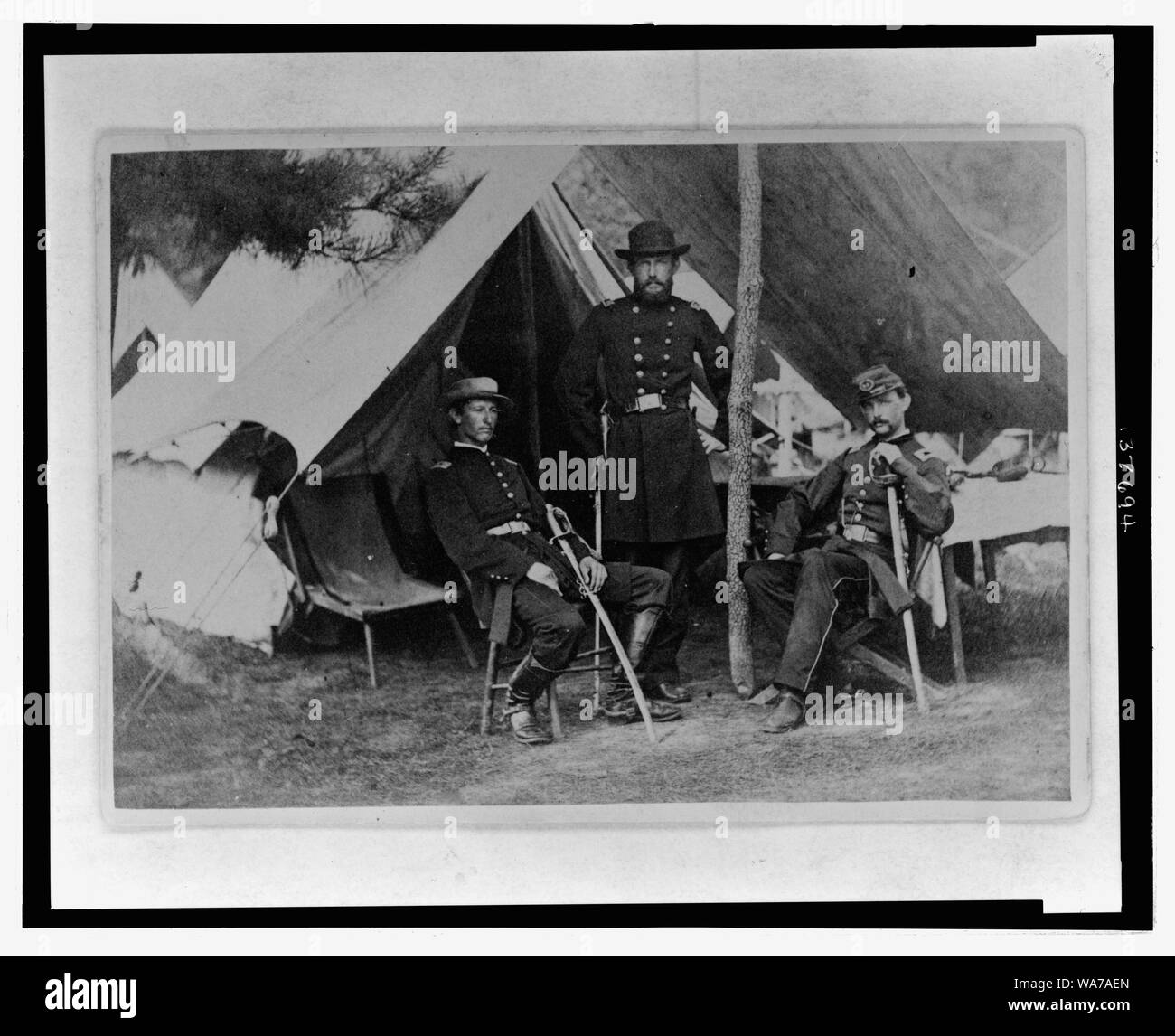 Albert J. Myer, U.S. Army Signal Corps officer di intera lunghezza verticale, rivolto verso la parte anteriore, in piedi sotto la tettoia di fronte ad una tenda, con una mano sulla cresta del palo con due uomini, uno seduto sulla sinistra e l'altra seduta sulla destra Foto Stock