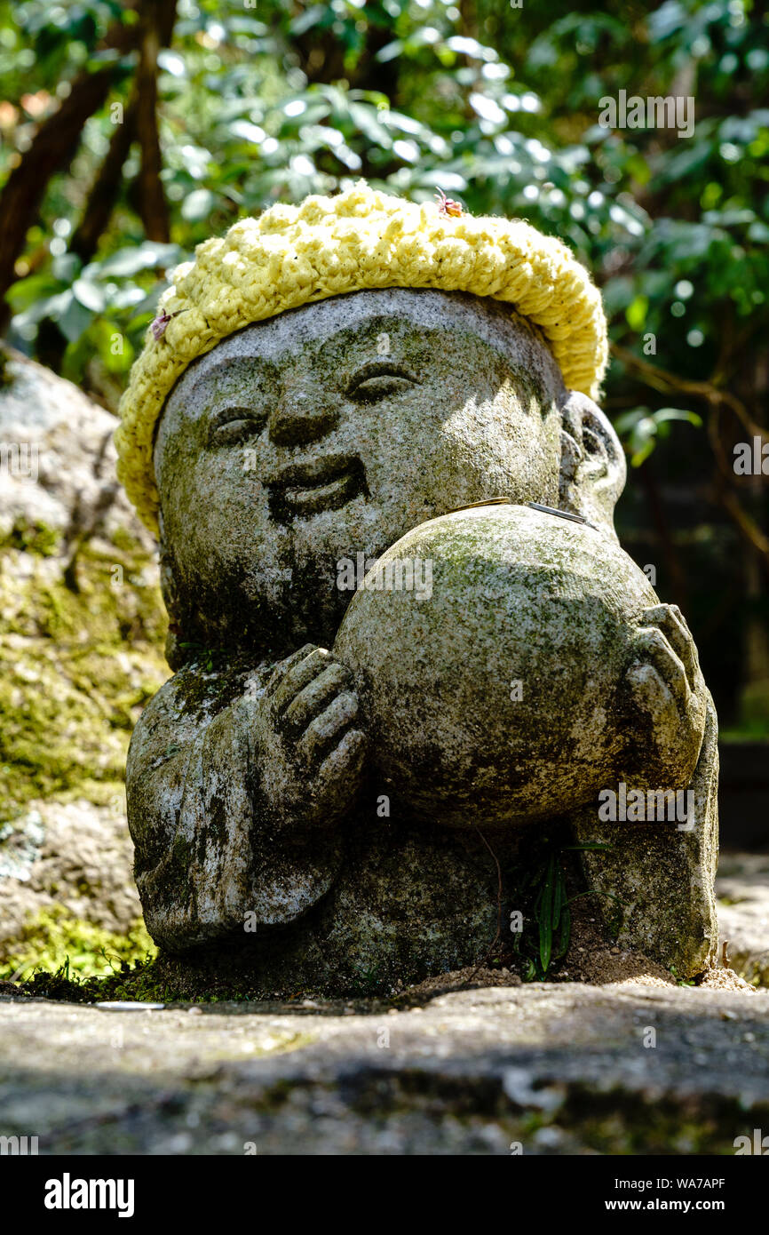Giappone, Miyajima. Tempio Daisho-in. Piccola statua Rakan di un monaco buddista, con cappello giallo di lana, che trasporta una grande palla di pietra in entrambe le mani. Foto Stock