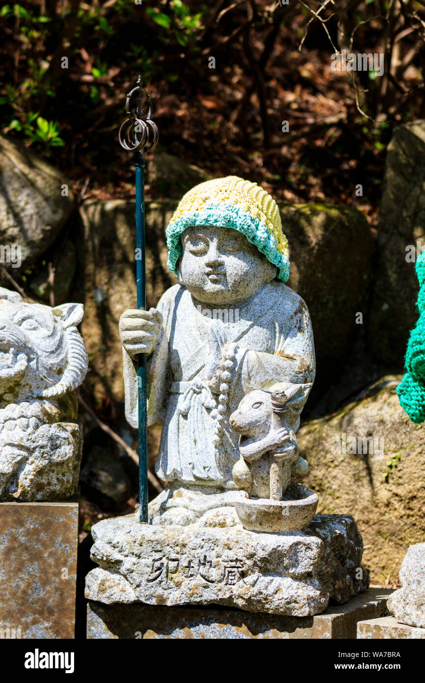 Giappone, Miyajima. Daisho-in. Piccola pietra Jizo statua di standing monaco buddista che trasportano un metallo shakujo con sei anelli. Il coniglio si inginocchia accanto a lui Foto Stock