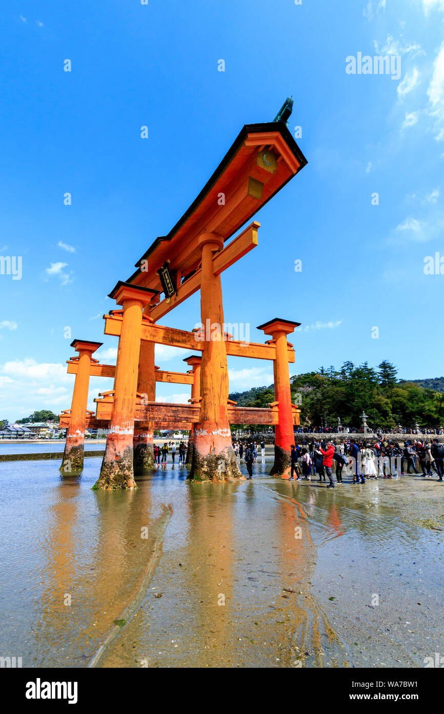 Giappone, Miyajima. Il grande Torii, o Otorii del santuario di Itsukushima. Red Torii sulla sabbia a marea e molte persone che camminano intorno ad esso. Foto Stock