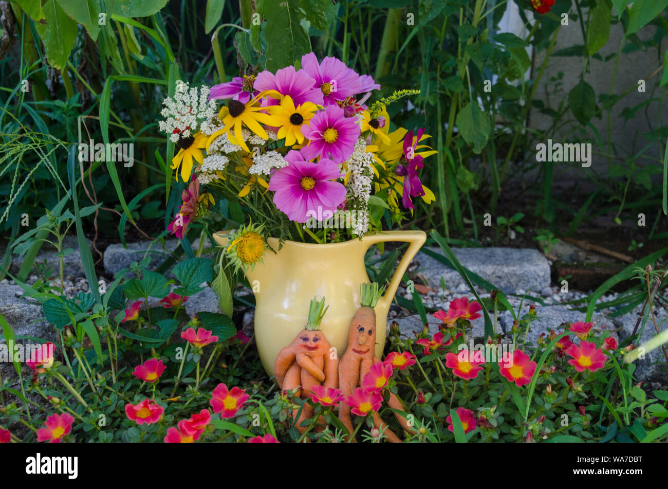Un maschio e femmina coppia di carote con facce dipinte di stare insieme in un giardino fiorito accanto al vaso di ceramica di fiori colorati, Yarmouth Maine, Stati Uniti d'America Foto Stock