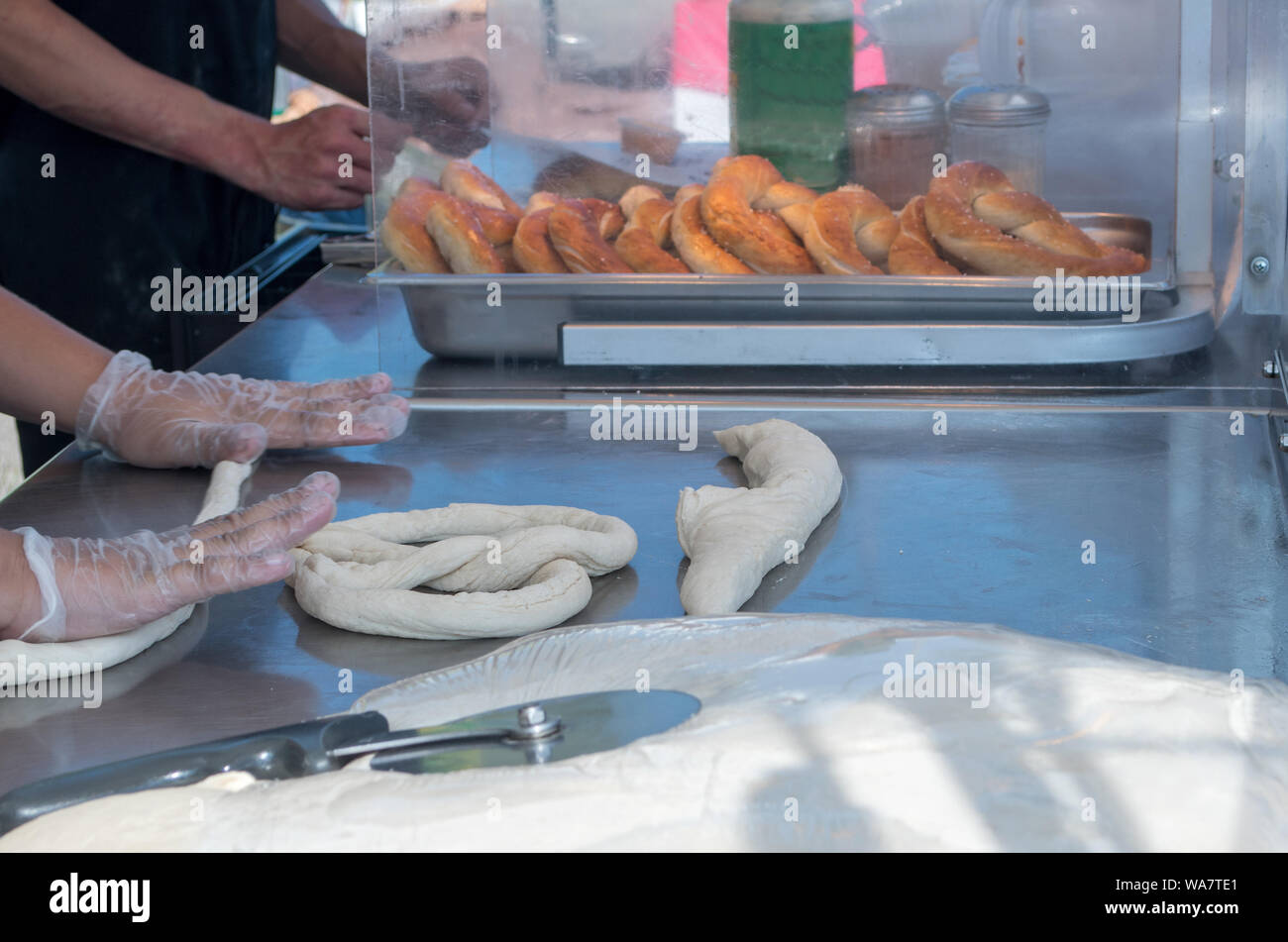 Baker a una fiera di strada, rendere piccante, pastosa pretzel per le persone di godere di pianura con mostarda, formaggio, dip o cannella e zucchero Foto Stock