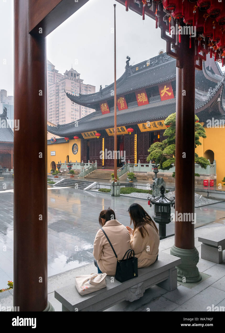 Due giovani donne si ripara dalla pioggia di fronte al Grand Hall presso il Tempio del Buddha di Giada, Shanghai, Cina Foto Stock