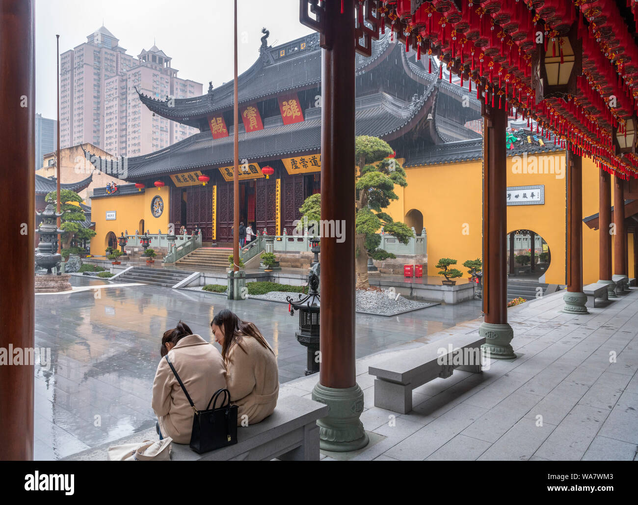 Due giovani donne si ripara dalla pioggia di fronte al Grand Hall presso il Tempio del Buddha di Giada, Shanghai, Cina Foto Stock