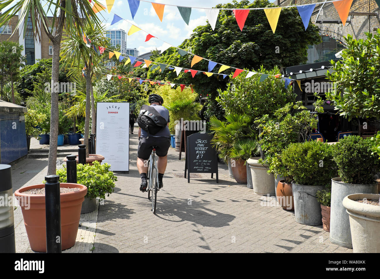 Un ciclista a cavallo la sua bicicletta sul marciapiede passato Jacks Thai Street food segno su Isabella strada nel sud di Londra SE1 Inghilterra Regno Unito KATHY DEWITT Foto Stock