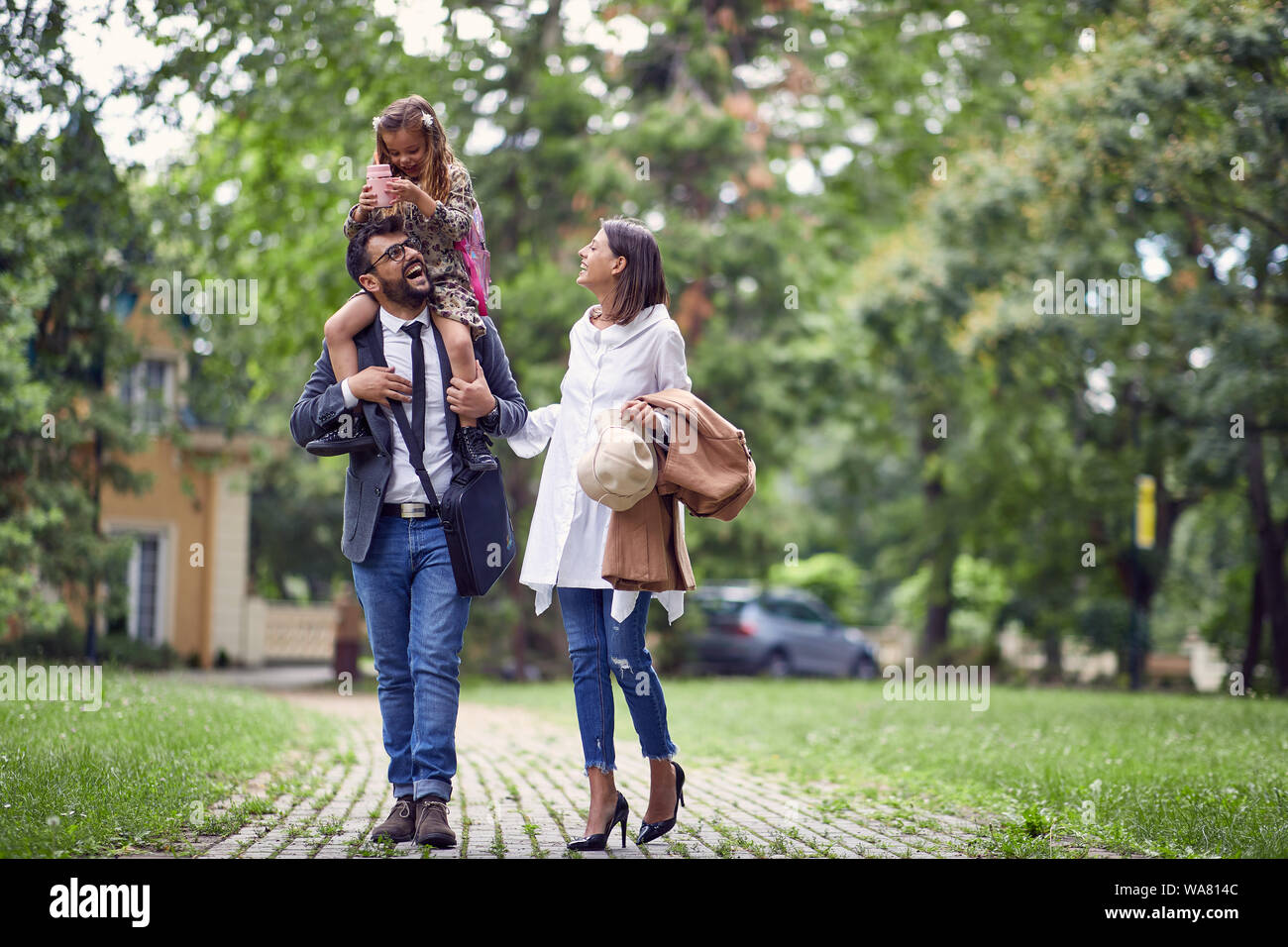 Famiglia sorridente a piedi a casa dopo il primo giorno di scuola Foto Stock
