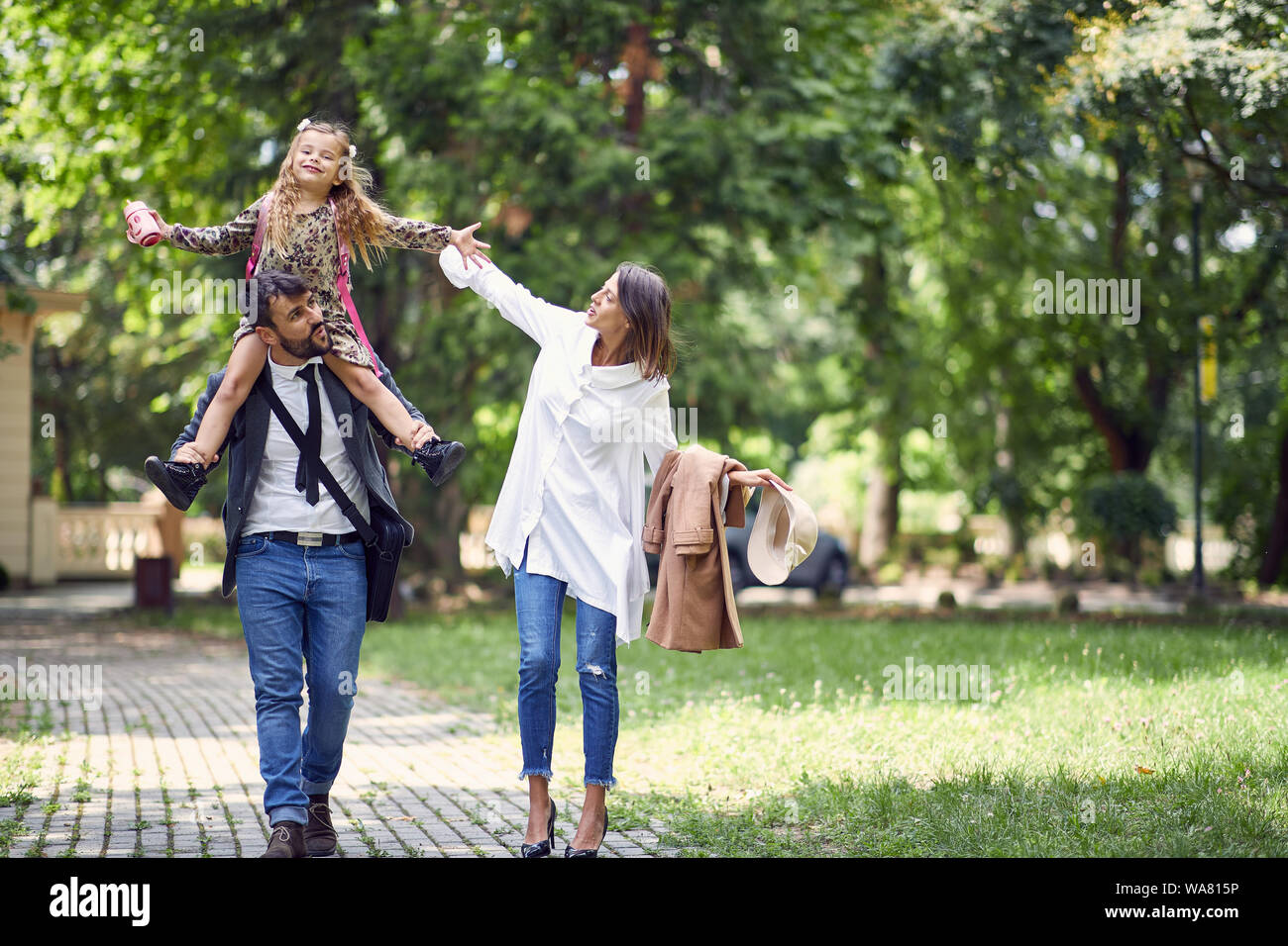 I giovani genitori a piedi con vi little schoolgirl throu park Foto Stock