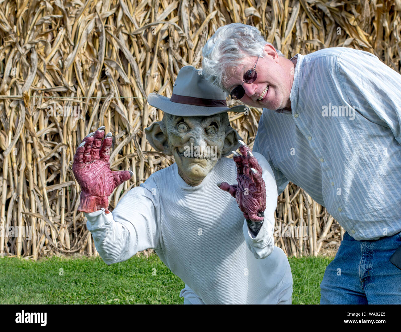 L'uomo pone con piccola statua indossa una maschera spaventoso, da un campo di mais Foto Stock