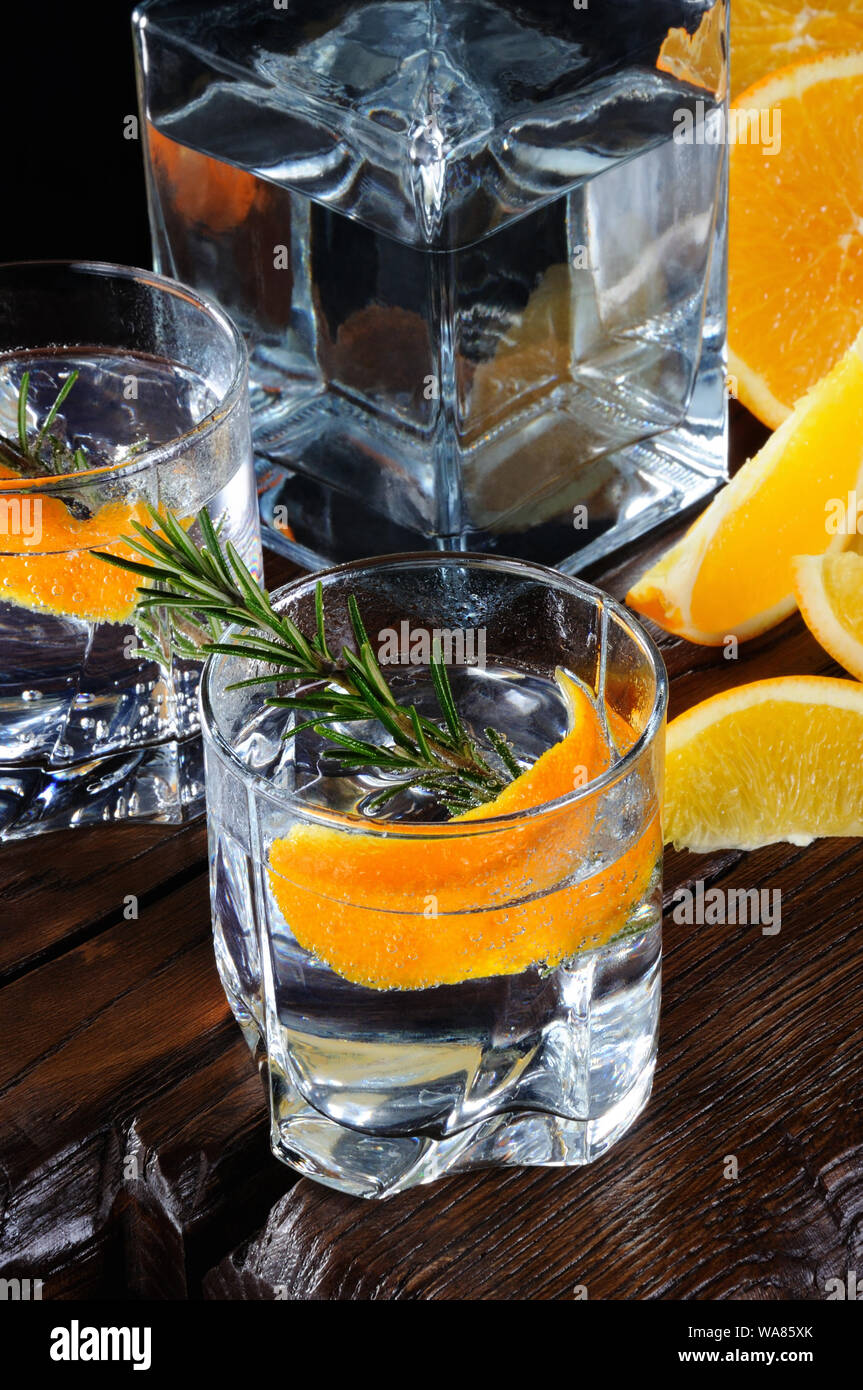 Cocktail classic dry gin con tonico e scorza di arancia con un rametto di rosmarino su una tavola di legno con fette di arancia succosa Foto Stock