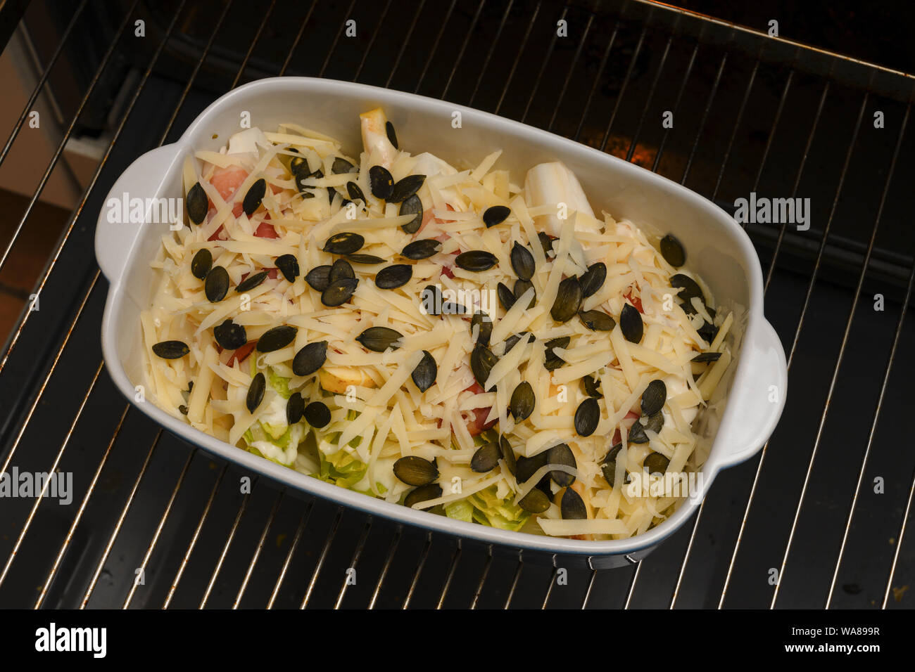 Preparate la cicoria o gratin di cicoria con Apple, prosciutto, formaggio e i semi di zucca in una casseruola su una griglia da forno pronto per il forno Foto Stock