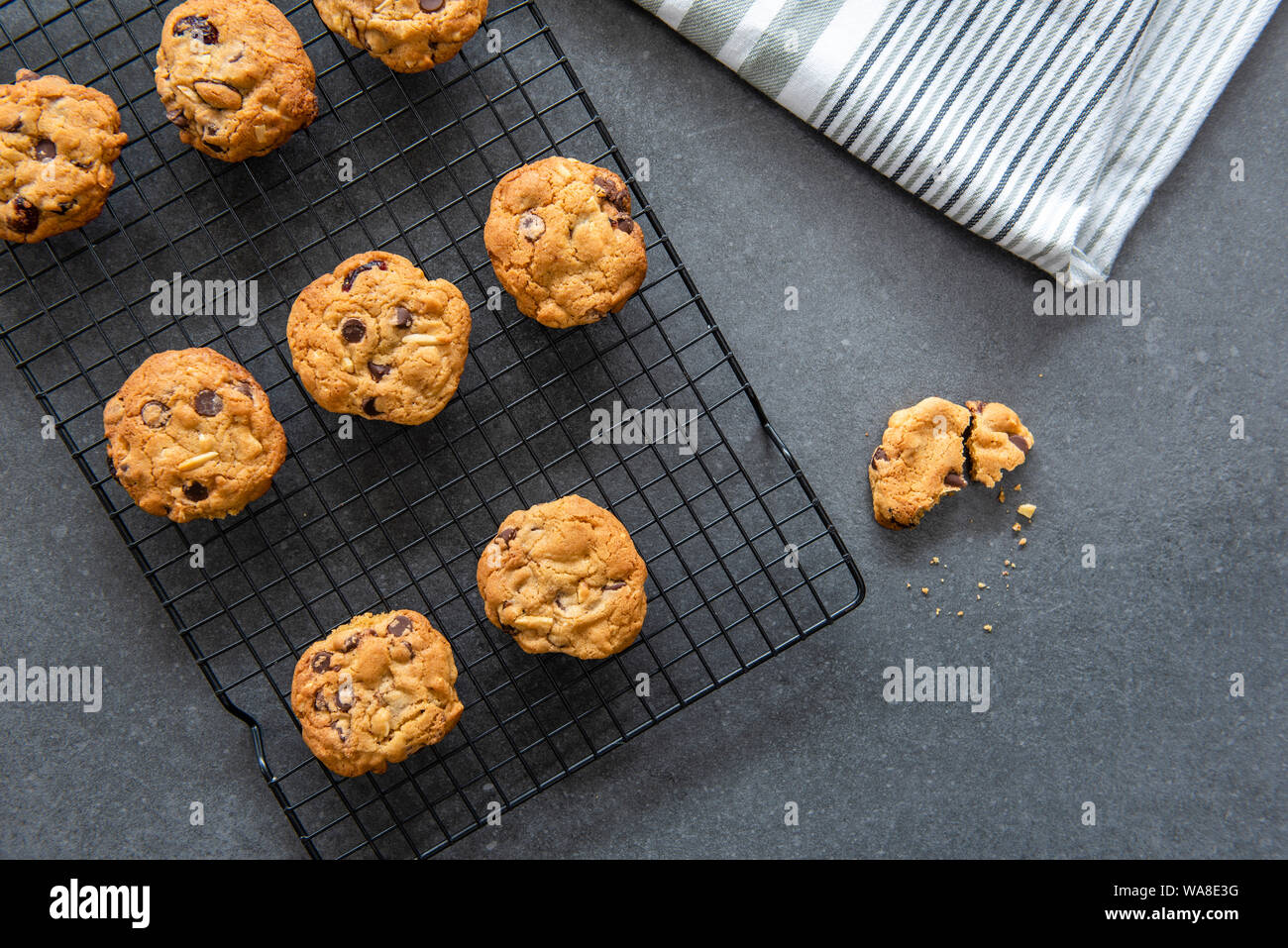 Pane appena sfornato in casa i biscotti al cioccolato con frutta e noci, mirtilli e mandorle, raffreddamento sul filo rack, sfondo scuro laici piatta Foto Stock