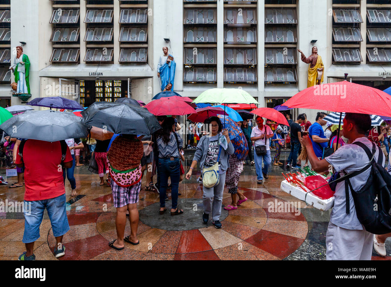 I Cristiani filippini attendere sotto la pioggia al di fuori di Quiapo Chiesa, Manila, Filippine Foto Stock