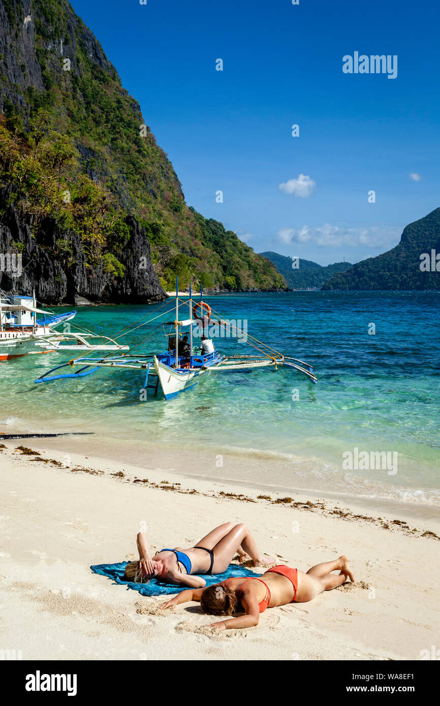 Turisti femmina a prendere il sole sulla spiaggia Pasandigan, El Nido, PALAWAN FILIPPINE Foto Stock