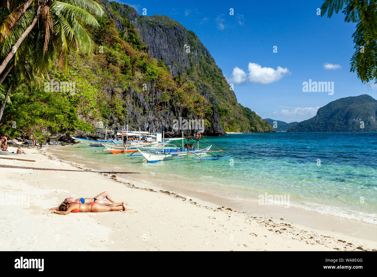 Turisti femmina a prendere il sole sulla spiaggia Pasandigan, El Nido, PALAWAN FILIPPINE Foto Stock