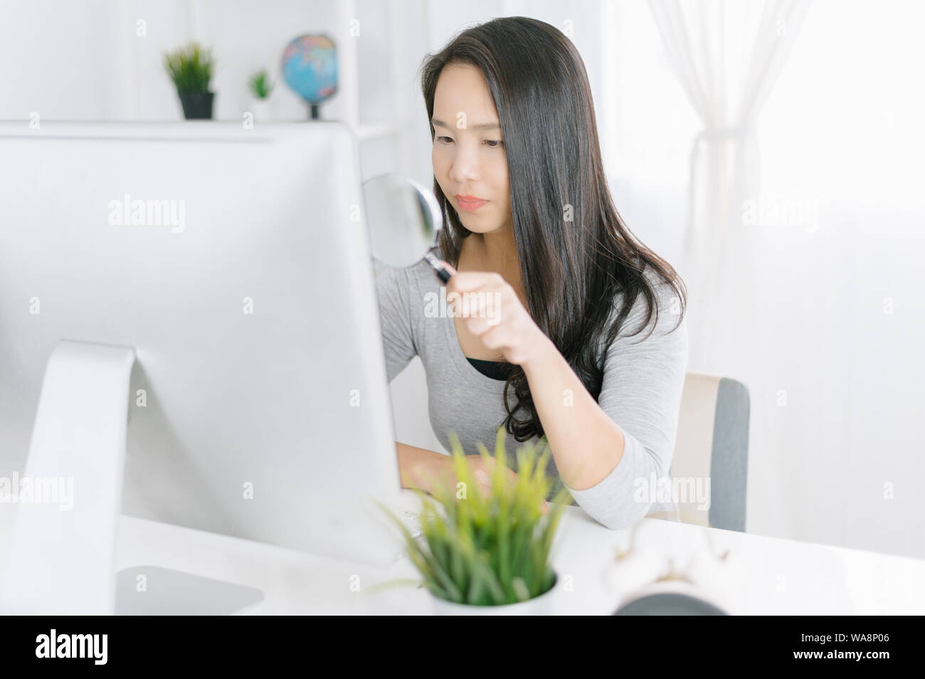 Donna con vetro magnifier esaminando un computer desktop .i file di scansione alla ricerca Trattamento Anti-virus di concetto Foto Stock