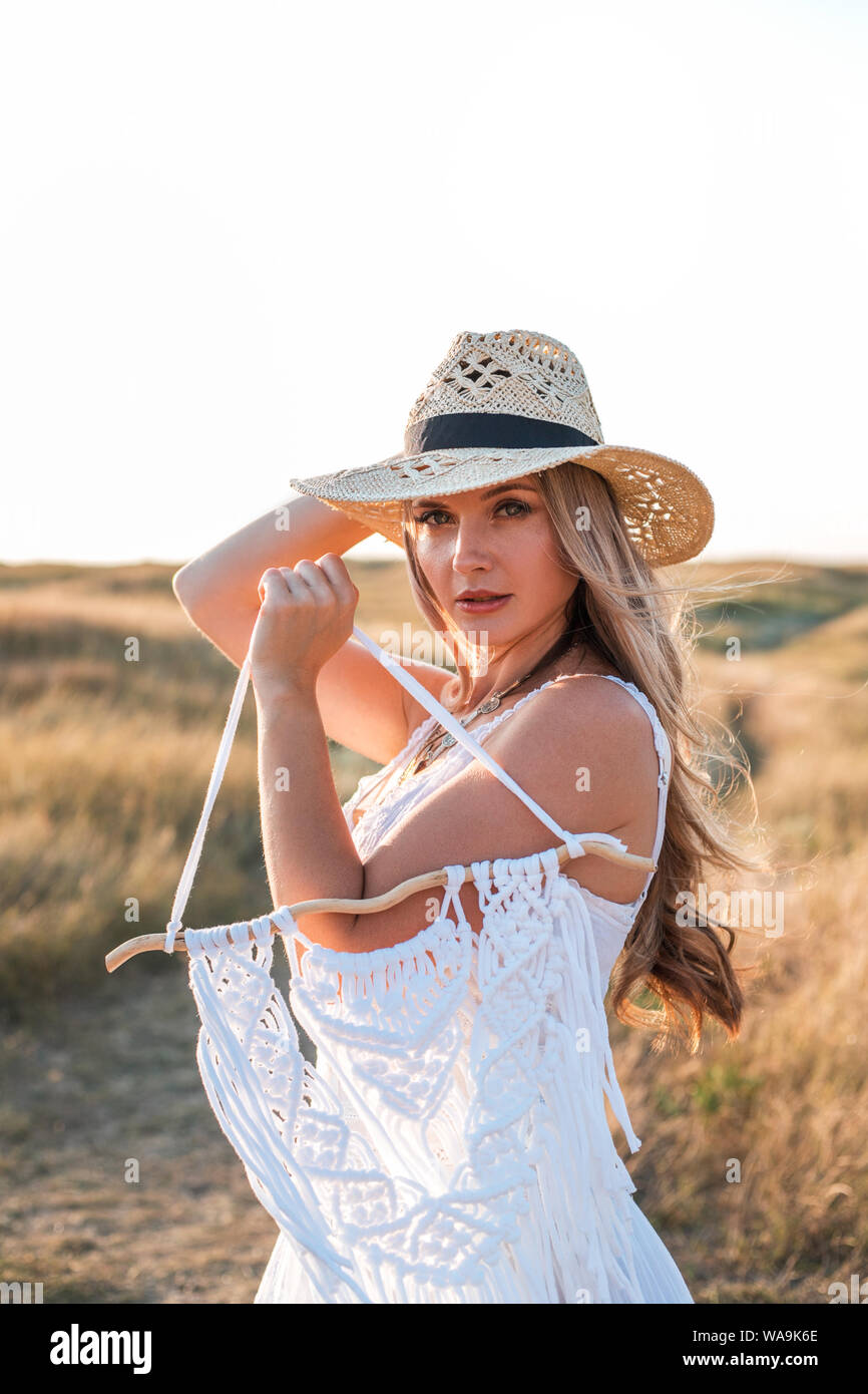 Bella donna che indossa in abito bianco e cappello di paglia per godersi la natura in esterni al tramonto. Foto Stock