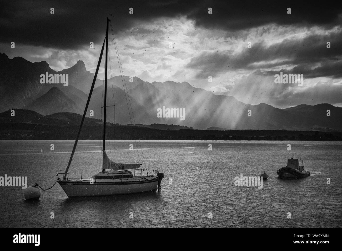 Gocce di pioggia e due barche su boe sul lago di Thun a pioggia con raggi solari e Stockhorn mountain range in background Foto Stock
